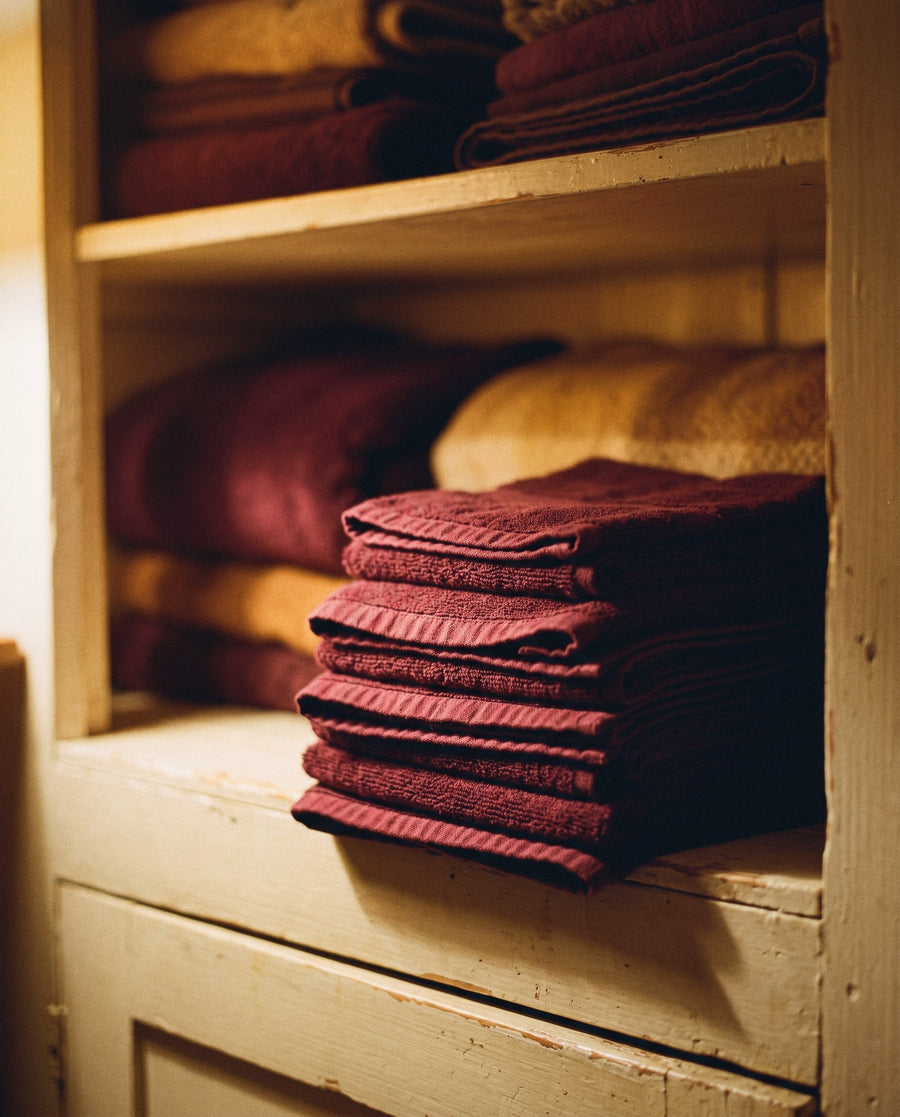 A stack of freshly laundered deep wine towels on a painted shelf in a linen cupboard, warm lamplight