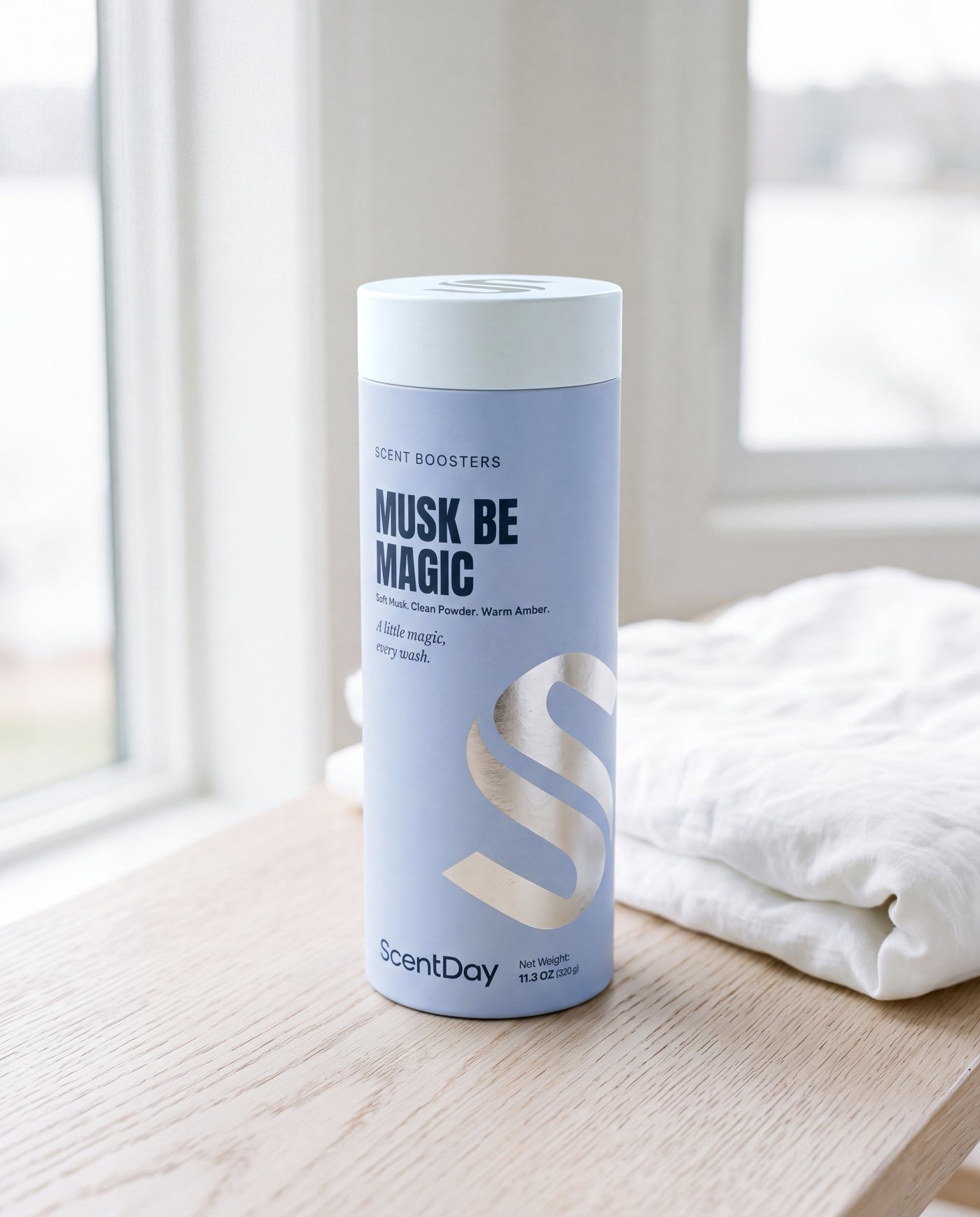 Musk be Magic scent booster tube in pale blue on a bleached oak bench beside folded white linen