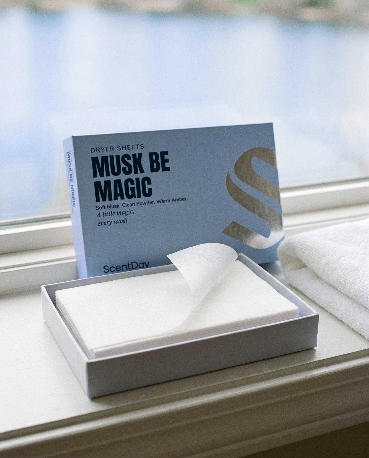 Open Musk be Magic dryer sheets box with a stack of white dryer sheets on a stone ledge