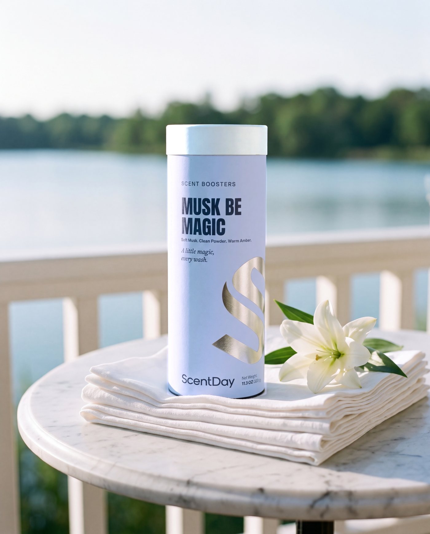 Musk be Magic scent booster tube on a stack of white linen with a white lily