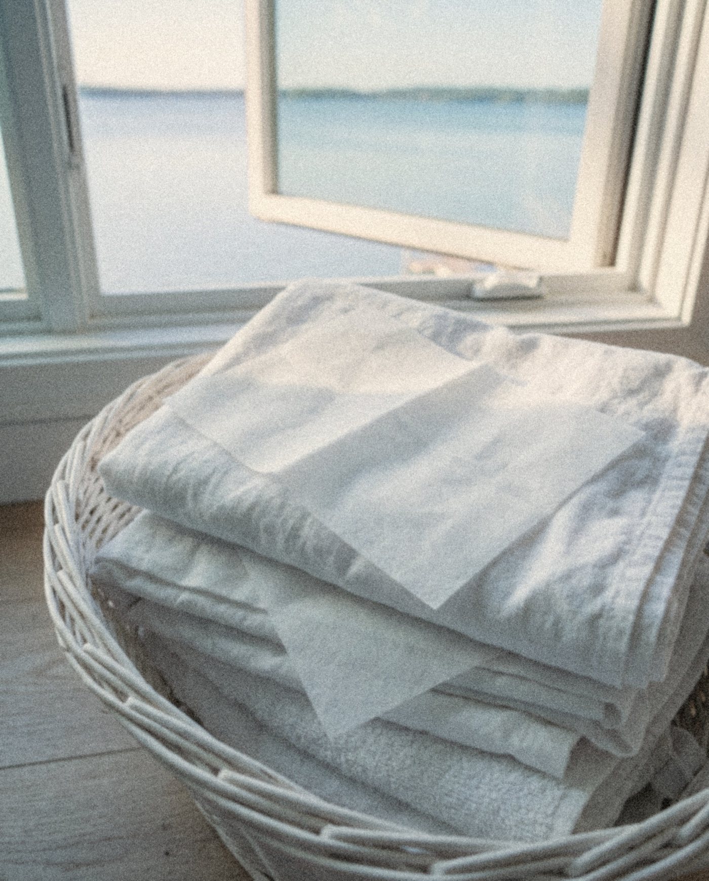 A white dryer sheet tucked into freshly folded towels in a basket by an open window over a lake