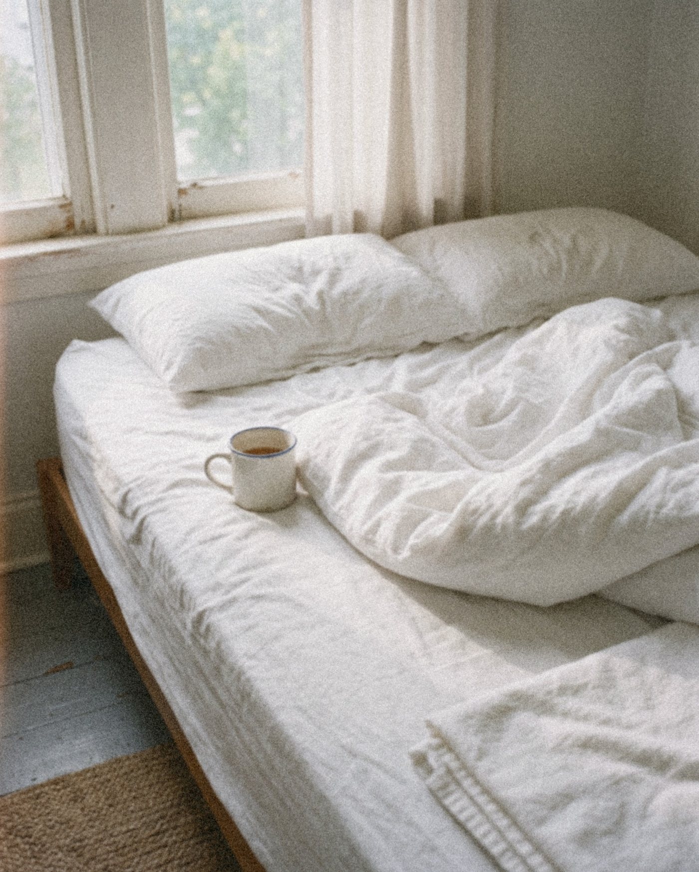 A freshly made white bed with a mug of tea in a quiet morning bedroom