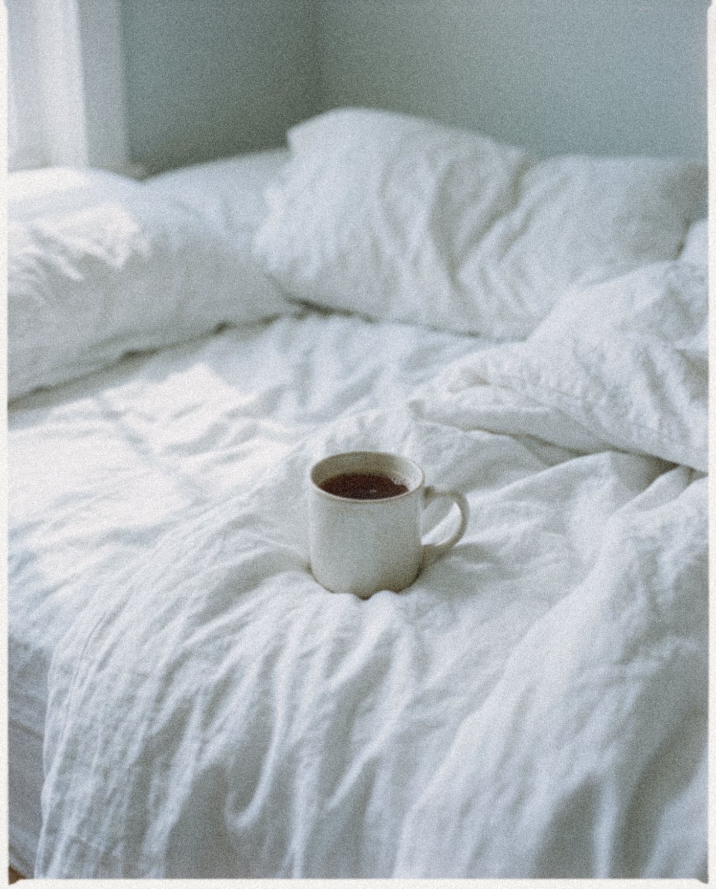 A mug of tea resting on a rumpled white duvet