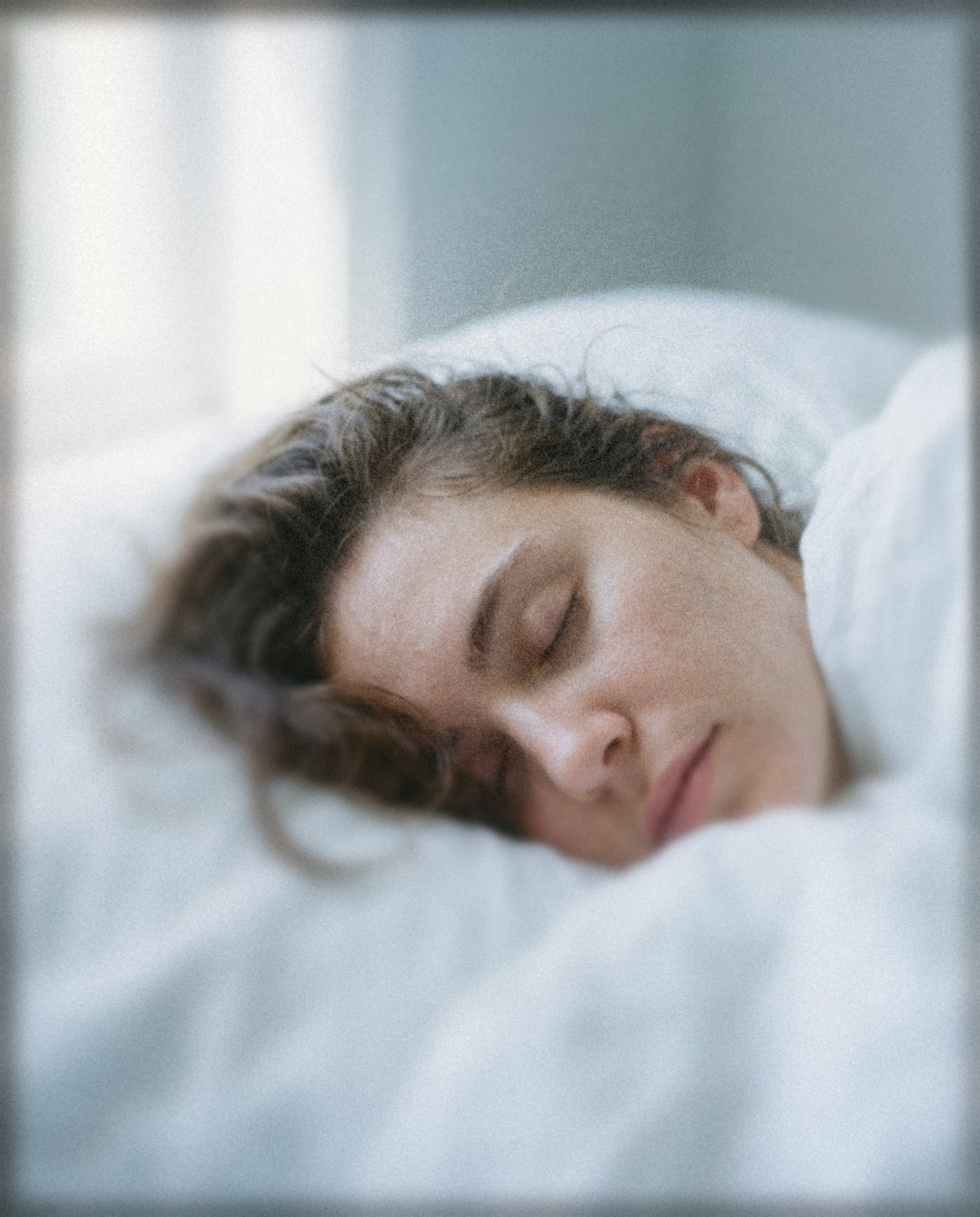 A woman asleep on a pale blue pillow in white sheets