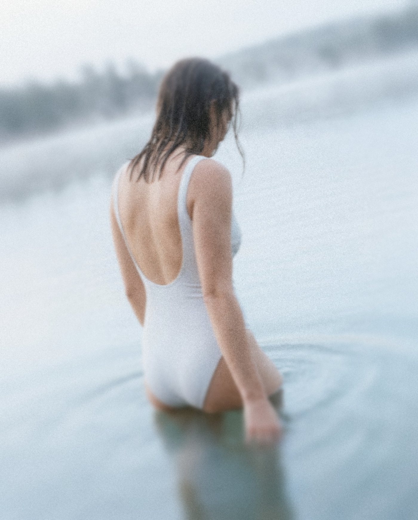 A woman in a white swimsuit wading into a misty lake in the early morning