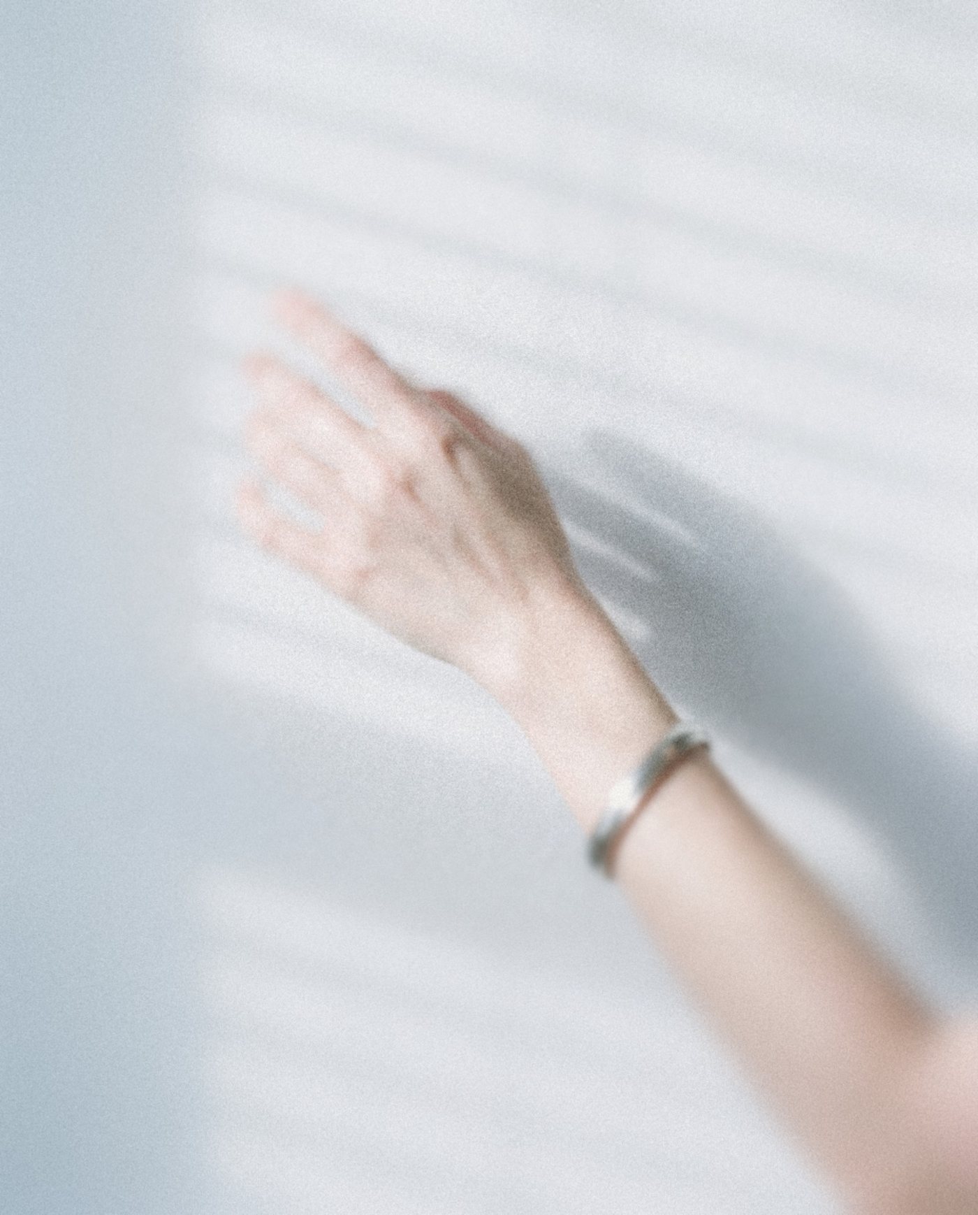 A raised wrist with a silver bangle against a wall striped with soft shadow