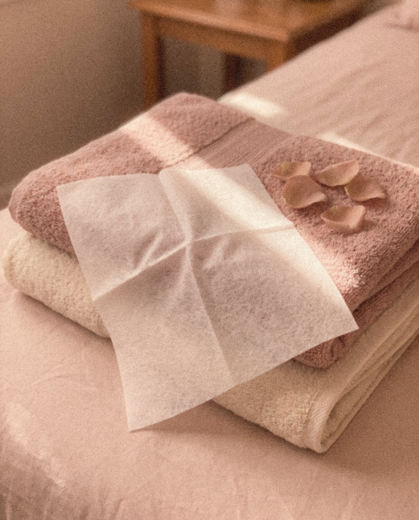 A white dryer sheet on folded blush towels scattered with rose petals