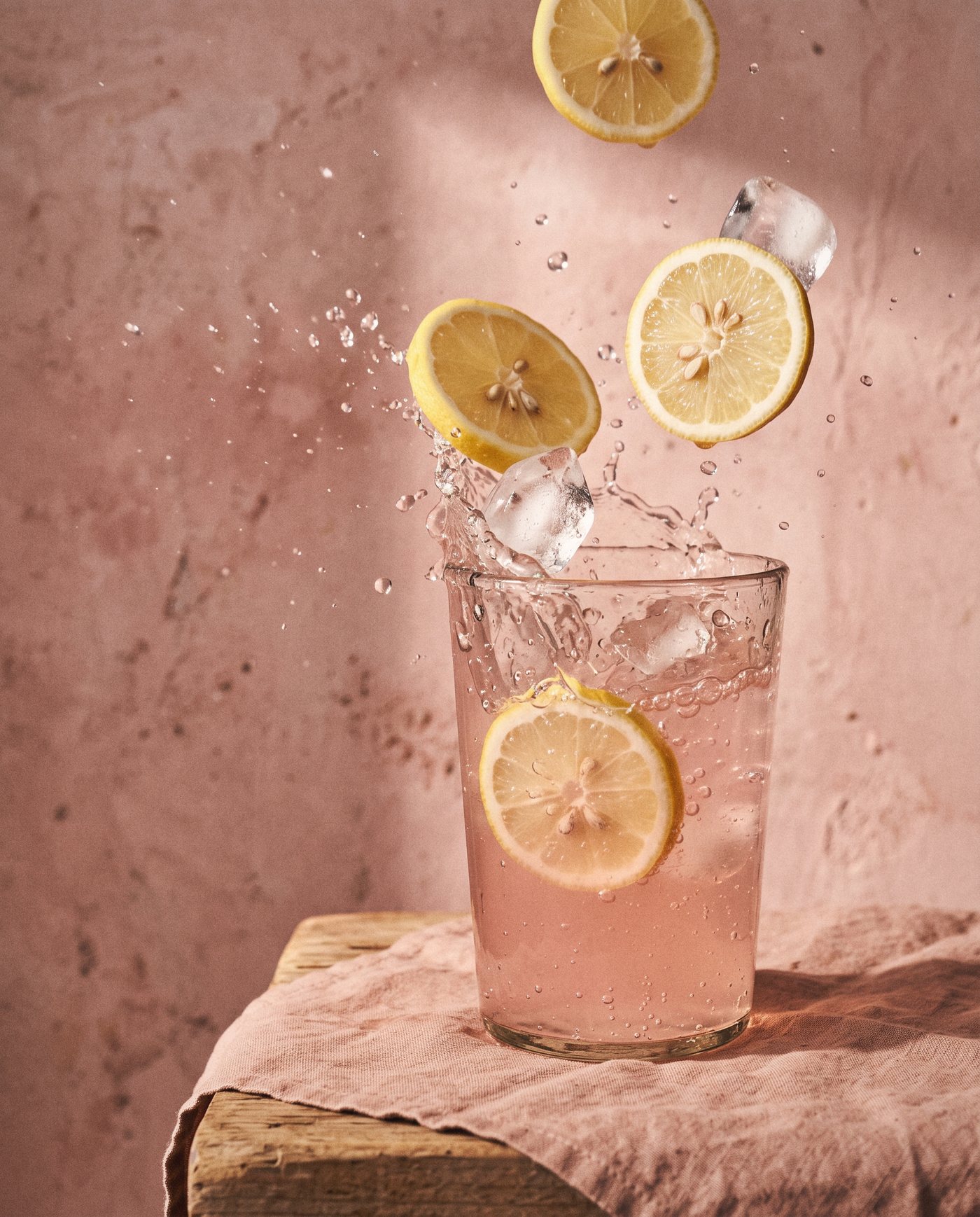 Lemon slices and ice splashing into a glass of pink lemonade