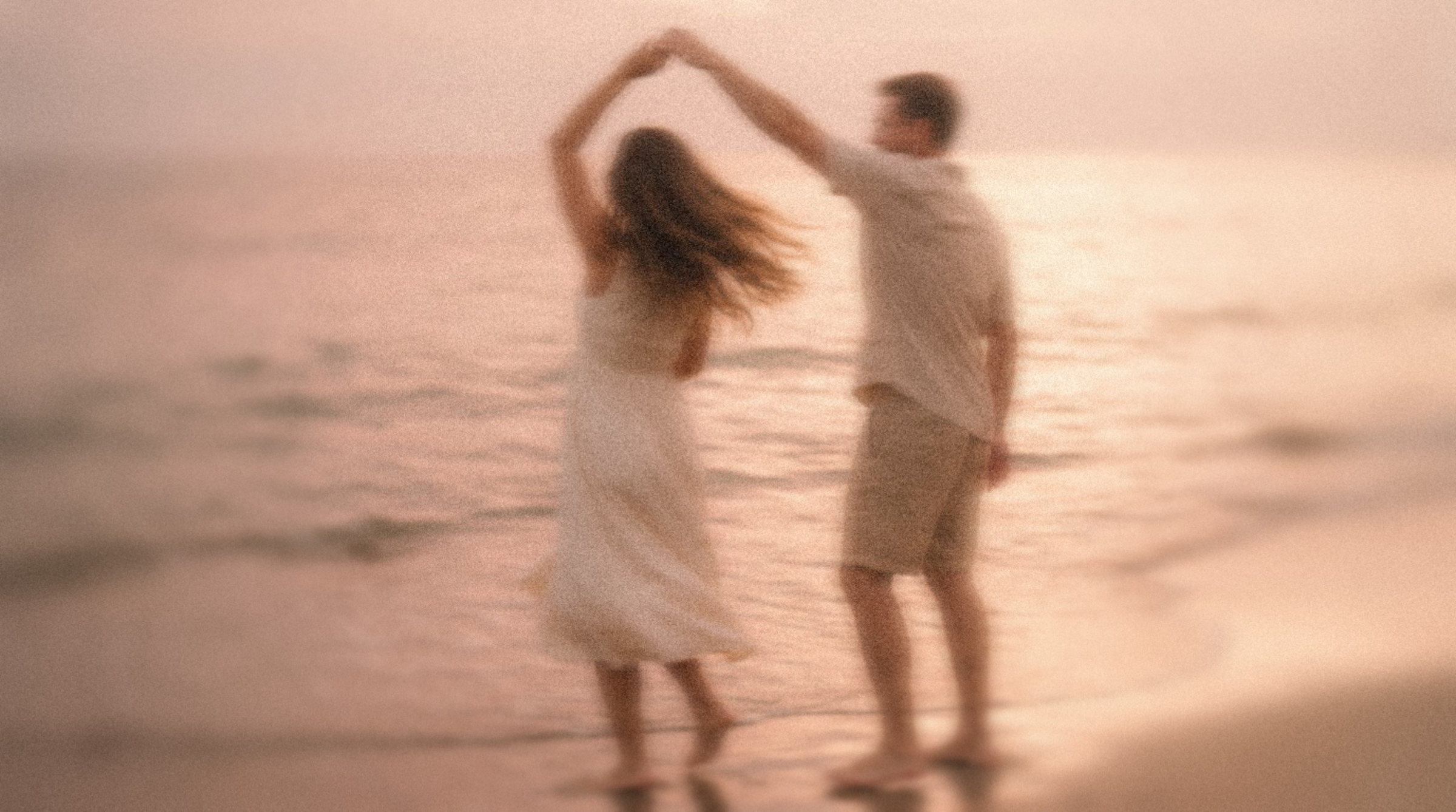 A couple dancing at the water's edge at sunset