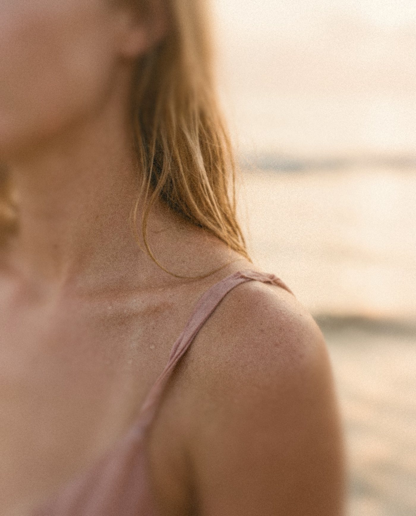 A sun-warmed shoulder with a blush slip strap by the sea
