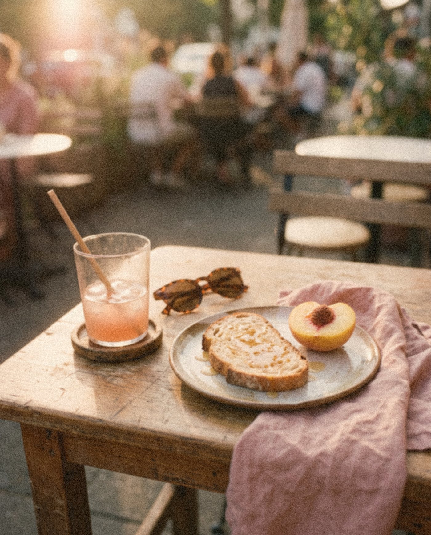 Breakfast at a café table in the sun: toast, a ripe peach and a pink drink