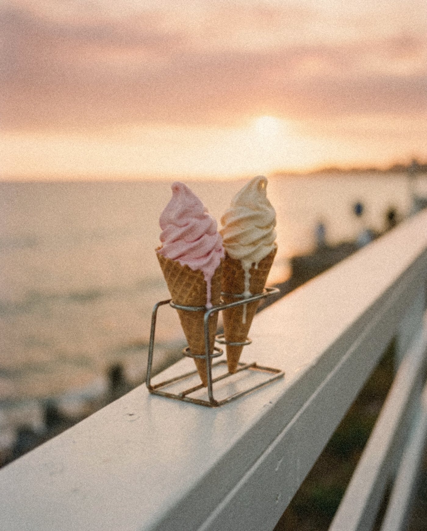 Two soft-serve cones on a white rail by the sea at sunset