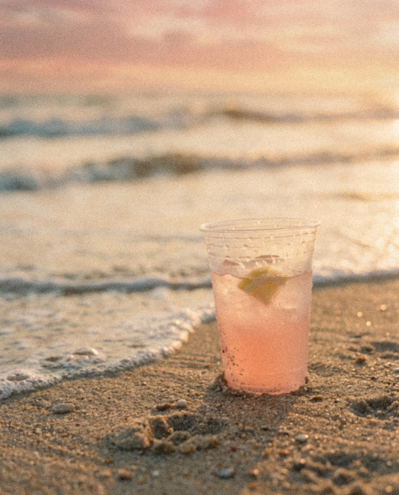 Pink lemonade in the sand at the water's edge at sunset